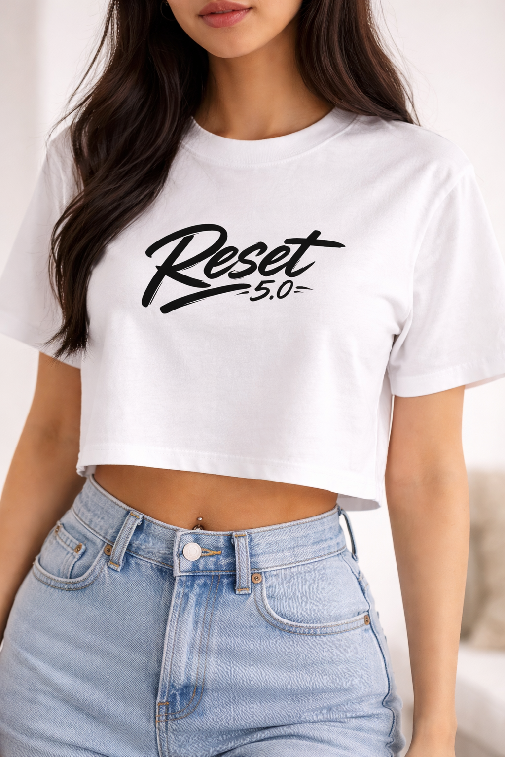 Person wearing a white crop top with 'Reset 5.0' text and light blue jeans.