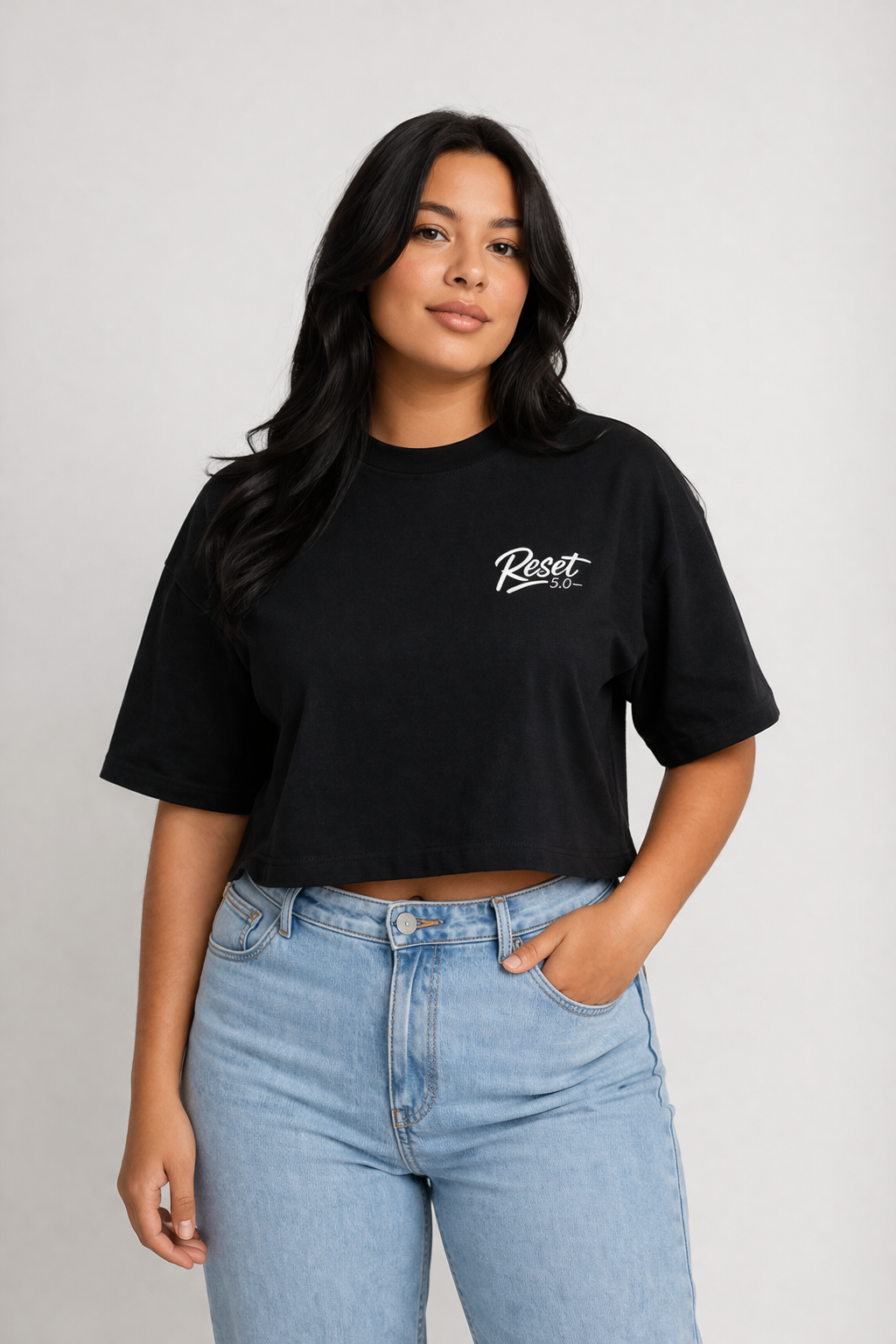 Woman wearing a black crop top with 'Reset' text and light blue jeans on a grey background